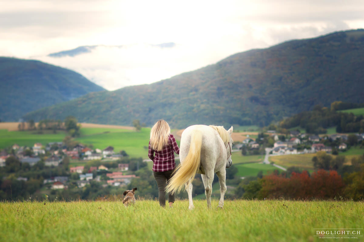 Femme qui part avec son cheval et son chien face aux montagnes